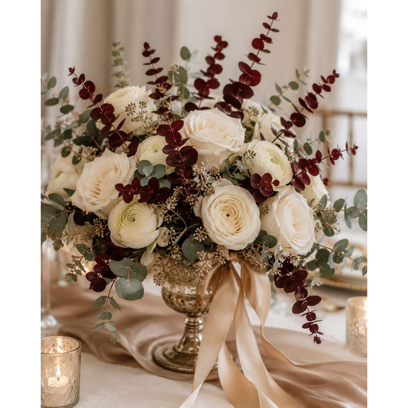 Decorative floral arrangement with white roses, red berries, and greenery on a table with candles.