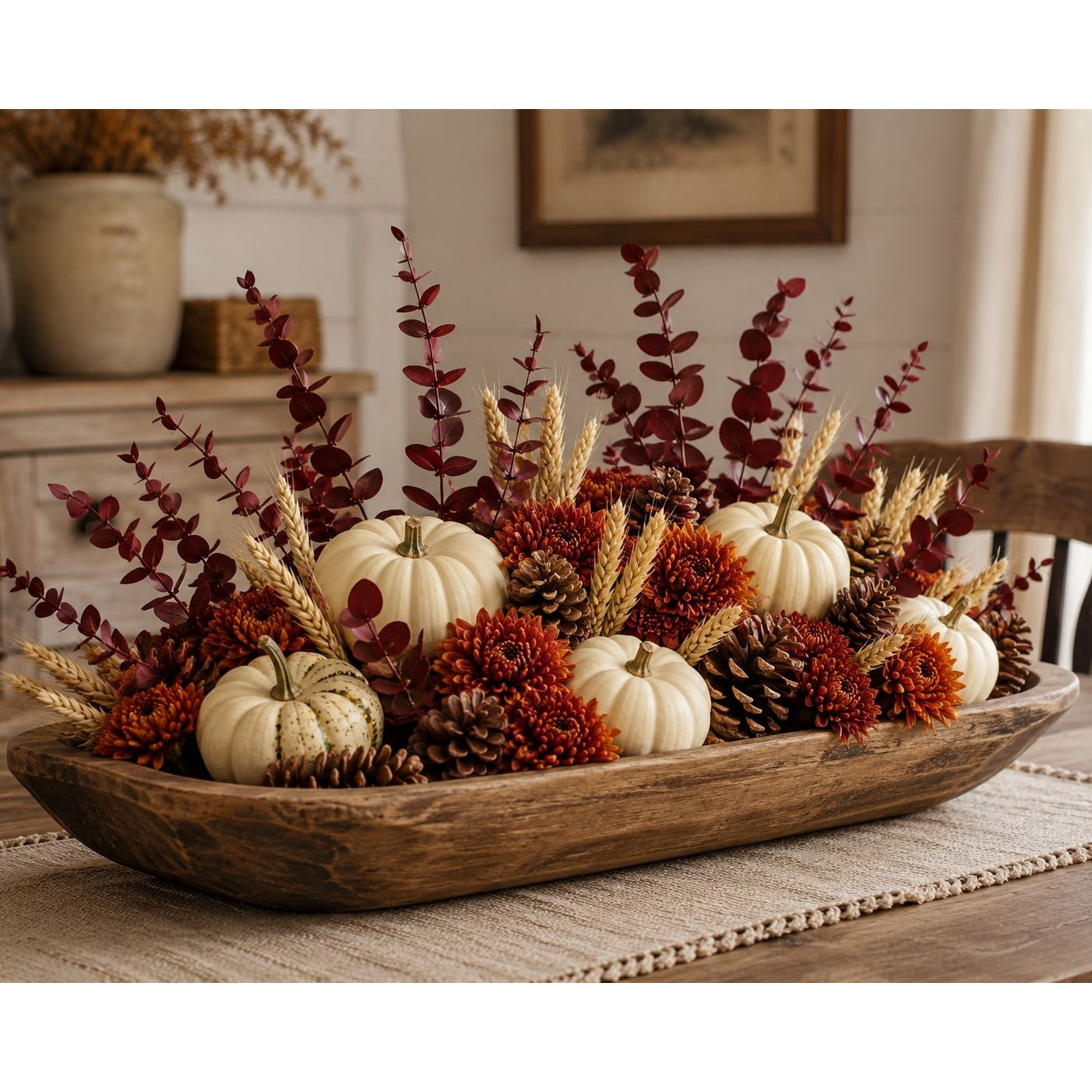 Decorative fall arrangement with pumpkins, leaves, and pinecones in a wooden bowl on a table.