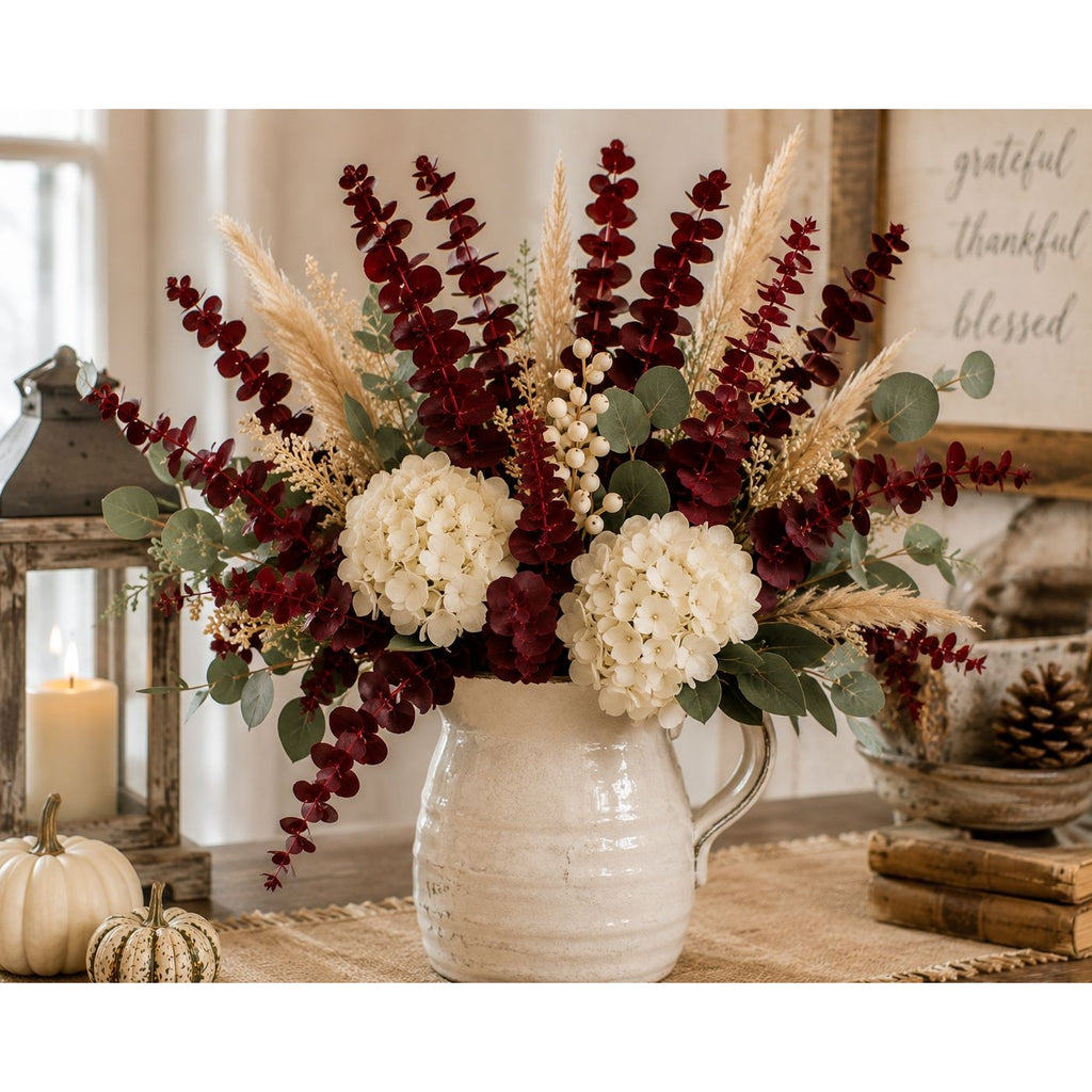 Autumnal floral arrangement in a white vase on a table with pumpkins and a lantern.