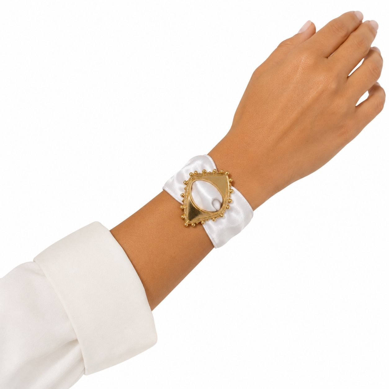 A gold-toned vintage-style eye-shaped brooch with a white satin ribbon loop, shown worn on a person's wrist against a white background.
