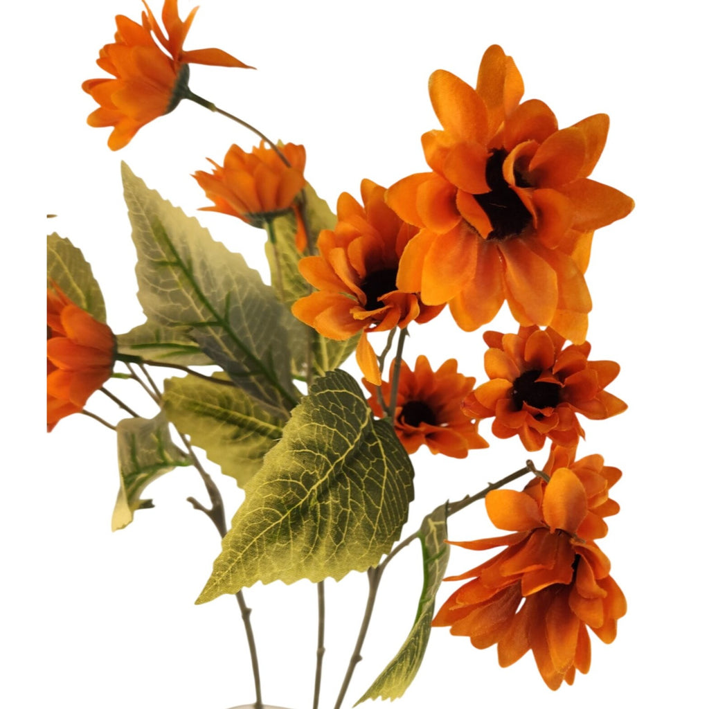 Orange artificial daisy-like flowers with dark centers and green leaves on a white background.