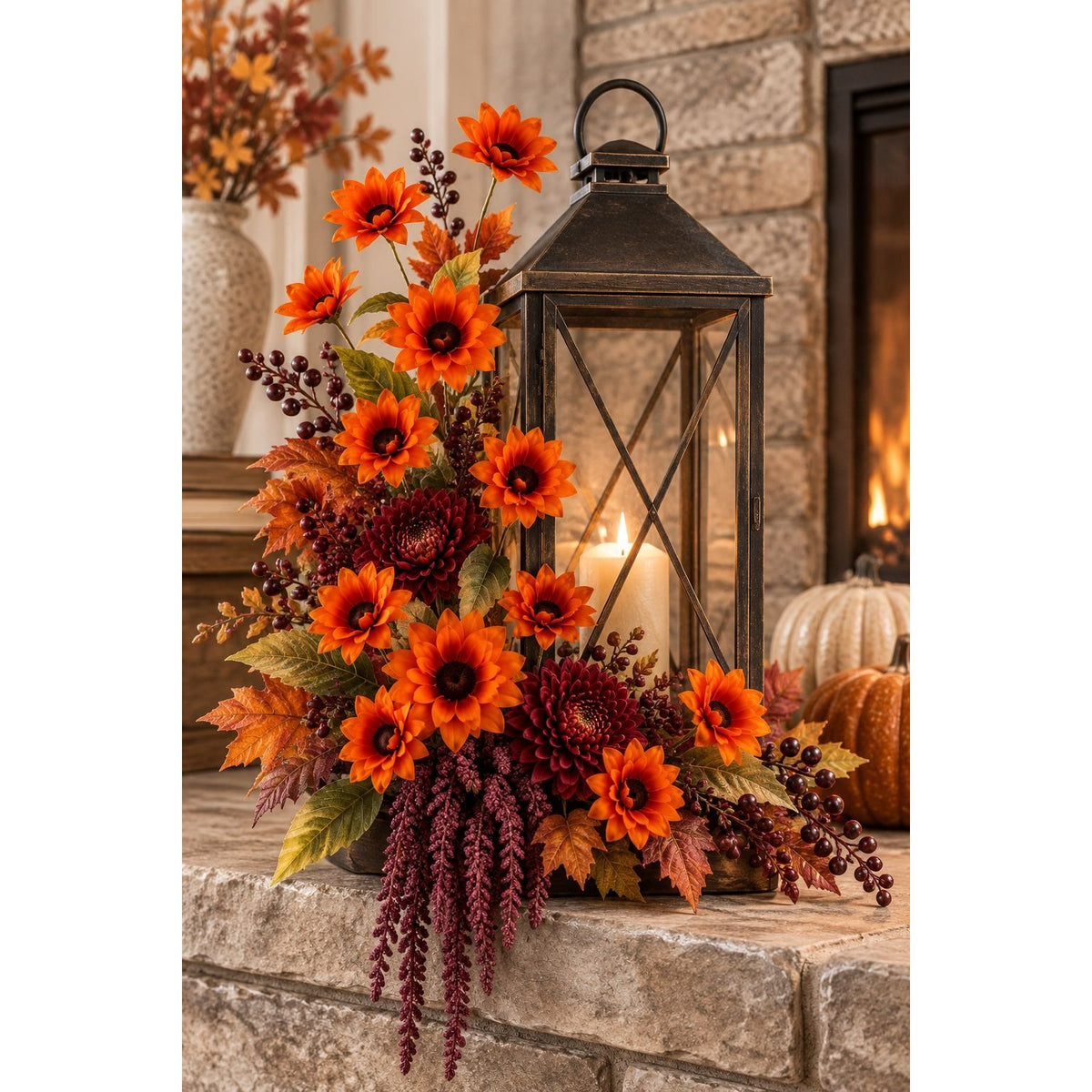 An autumn floral arrangement with bright orange flowers, burgundy berries, and fall leaves, styled beside a black lantern on a stone fireplace ledge with pumpkins and a warm fire in the background.