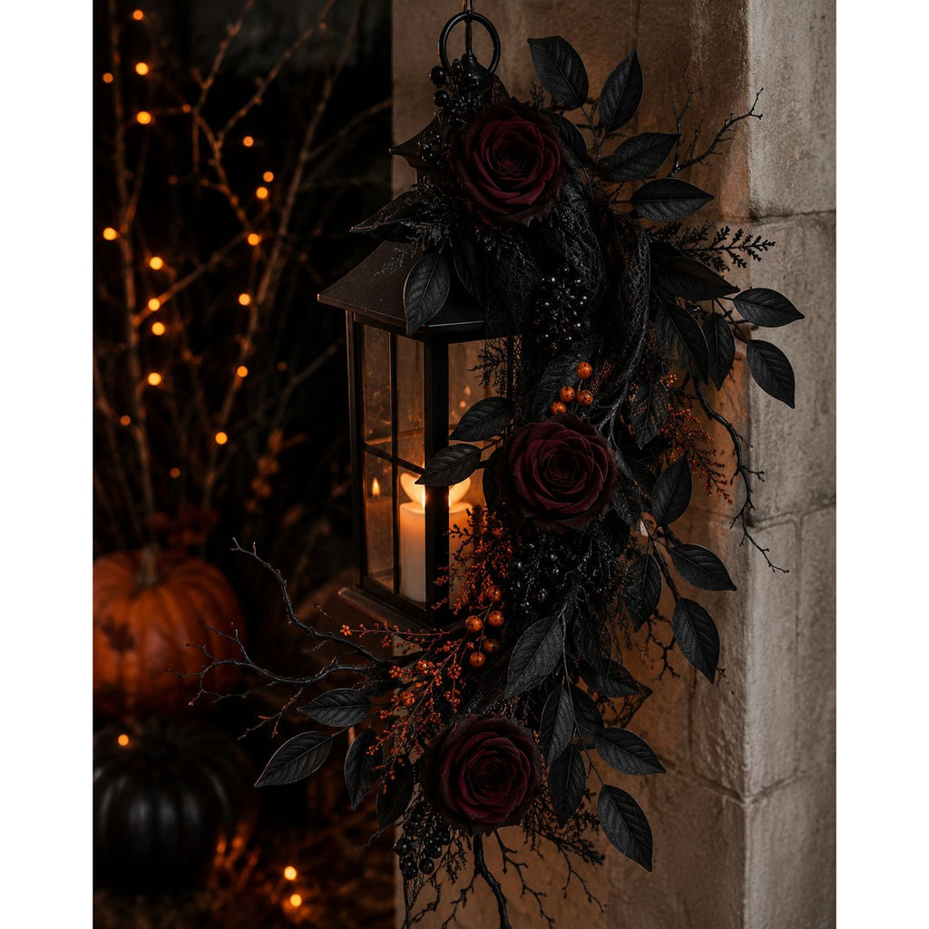 Decorative lantern with roses and leaves on a stone wall with pumpkins and string lights in the background.
