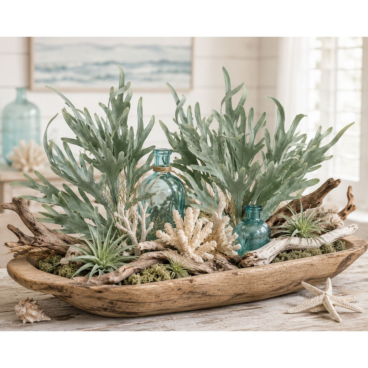 Decorative arrangement with green plants, corals, and a wooden bowl on a table.