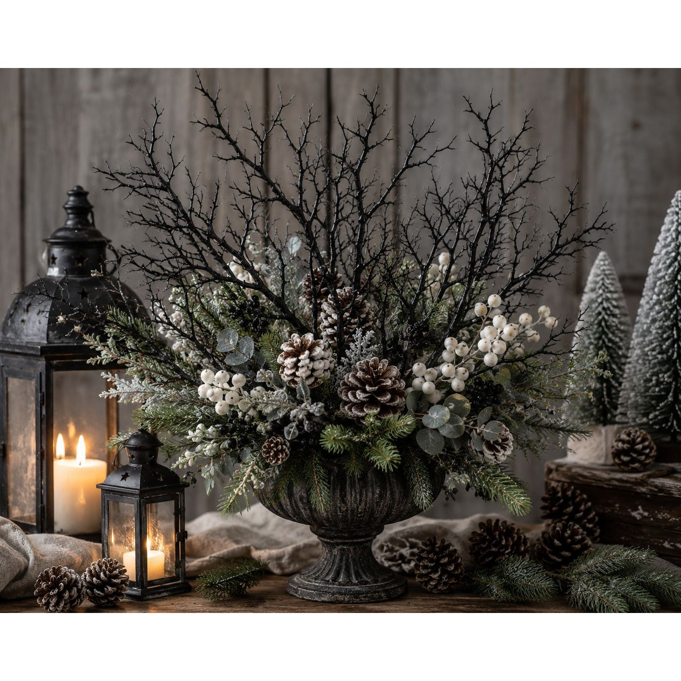 Decorative arrangement with branches, flowers, and pinecones in a vase, surrounded by lanterns and small trees.