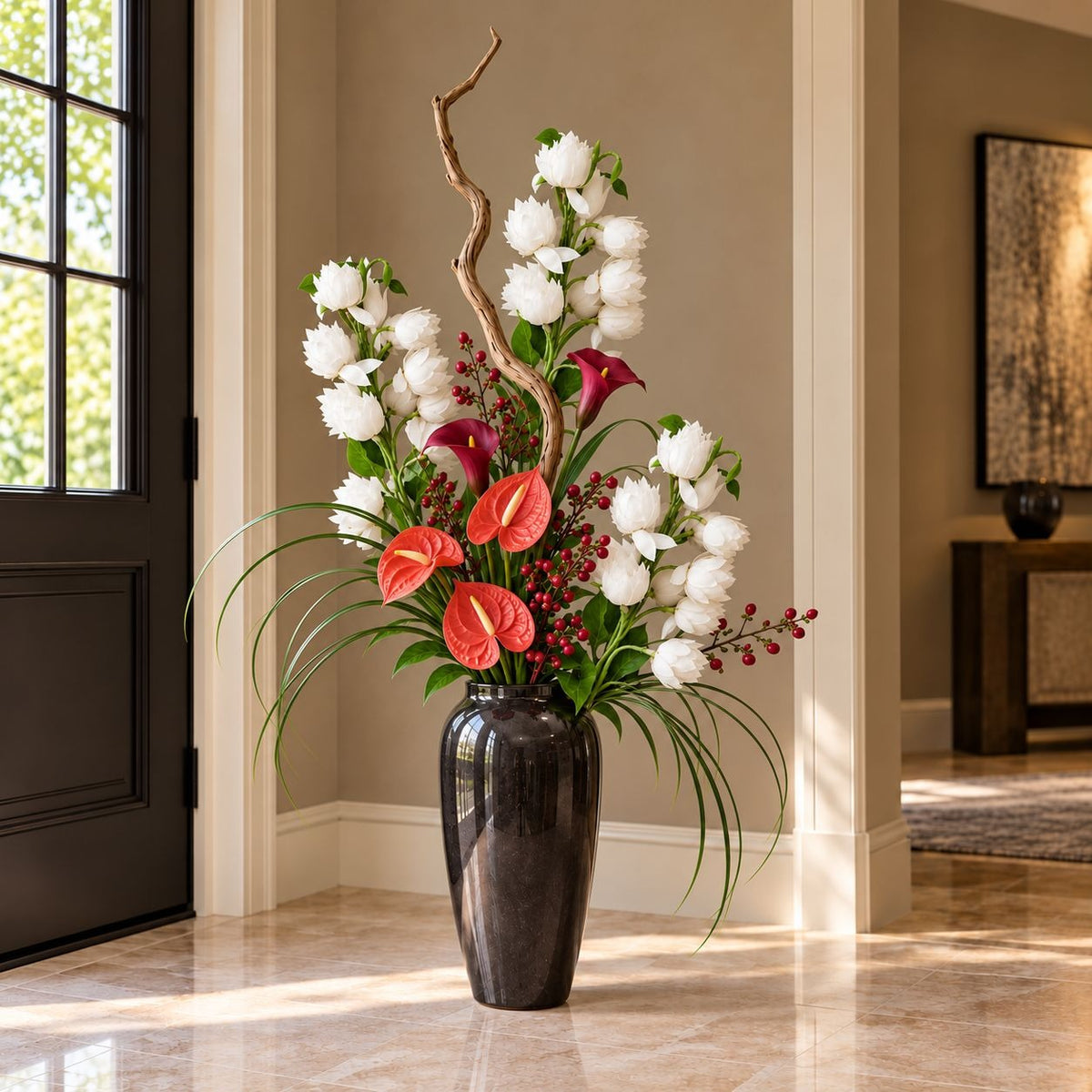 A large black ceramic vase filled with a vibrant floral arrangement featuring white peonies, red anthuriums, red berries, and green foliage, placed in a bright entryway next to a black door.