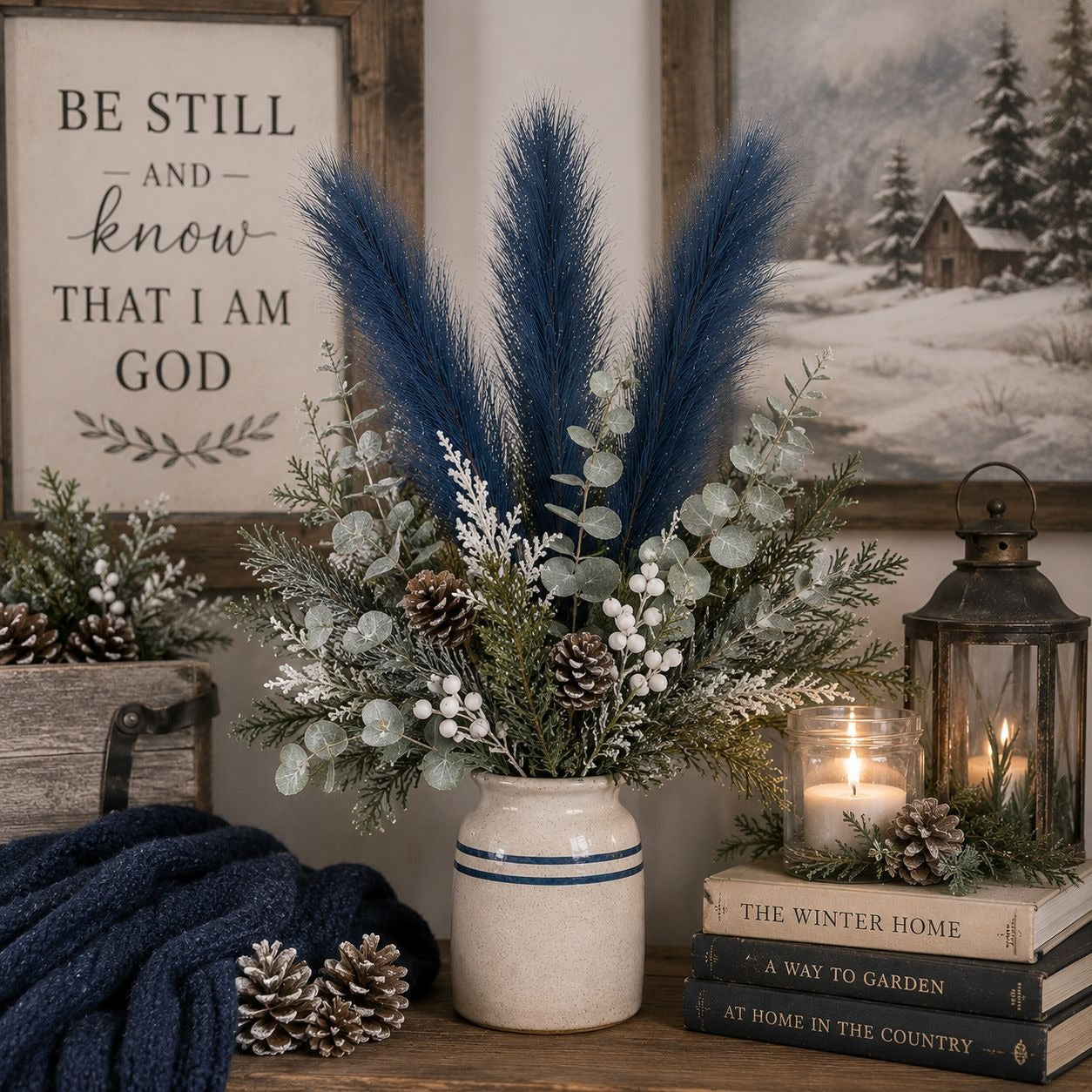 Decorative arrangement with a vase of blue and green pampas grass, candles, and books on a wooden surface.