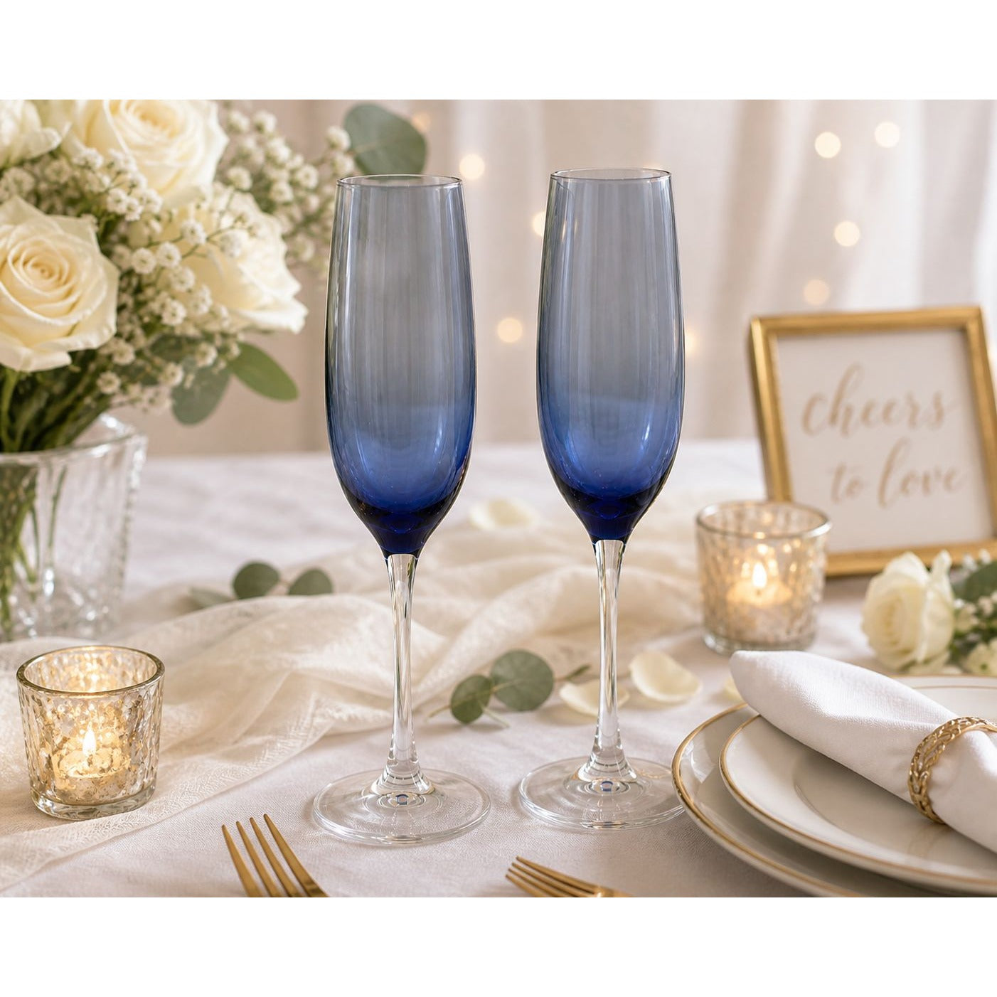 Two blue champagne flutes on a decorated table with candles and flowers.